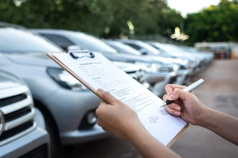 Action of a customer is signing on the agreement term of car rental service. Close-up and selective focus a human's hand with blurred background of cars in a row.