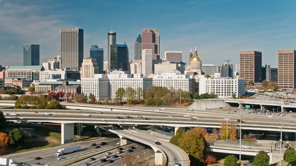 Aerial shot of the interchange between Interstate 85, Interstate 20 and multiple surface streets with downtown Atlanta office towers and the Georgia State Capitol beyond on a sunny afternoon in Fall.
