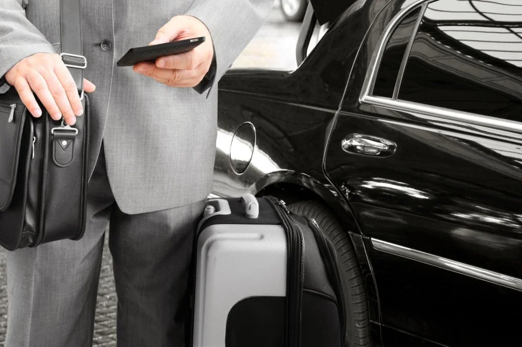 Businessman standing by a car with his luggage while calling by his phone with car service in Washington DC