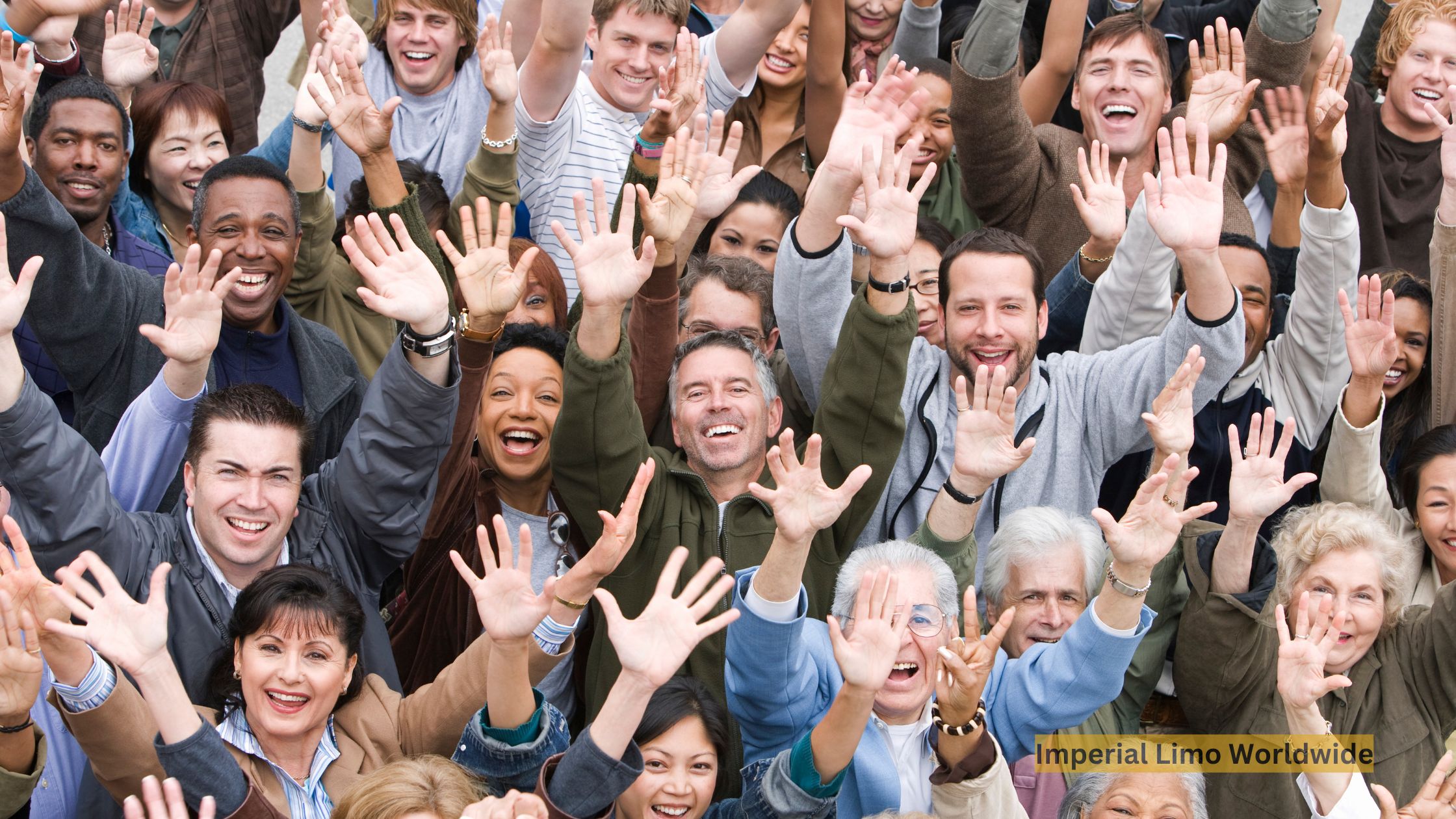 A large, joyful crowd of people seen from above, smiling and raising their hands together at an event.