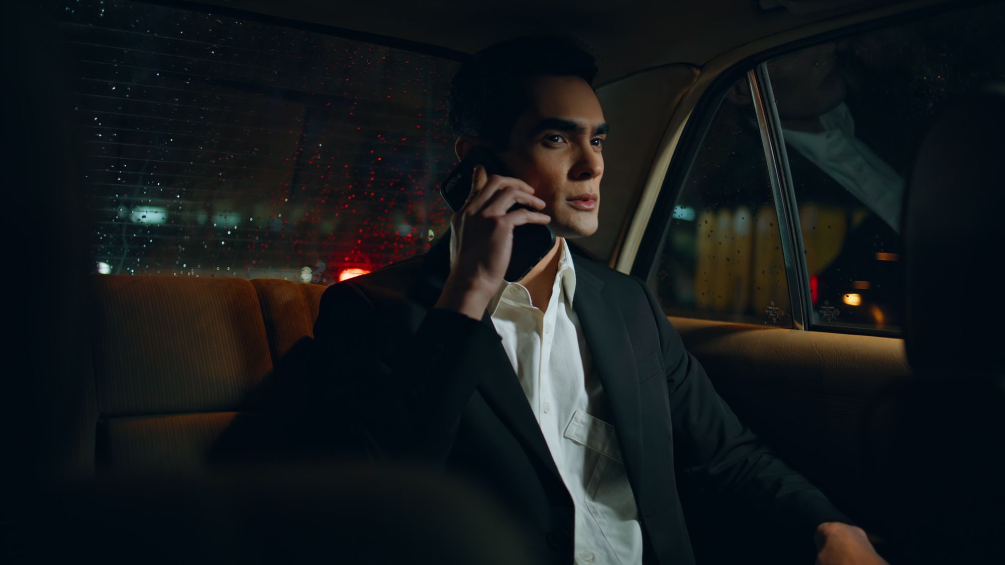 Passenger on the phone in the back seat of a chauffeured car at night