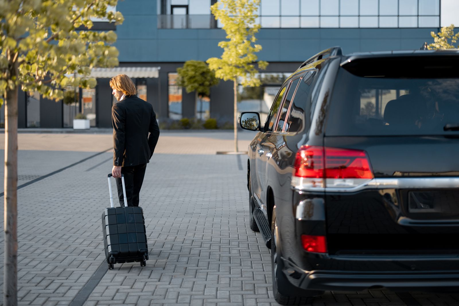 Traveler with a suitcase walking to a black SUV for a chauffeured airport pickup
